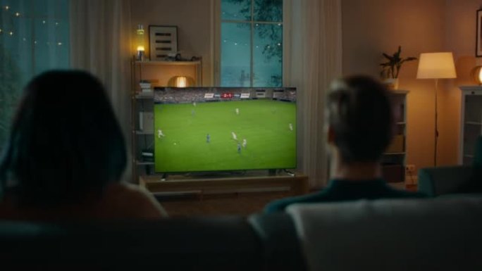 白人足球迷夫妇晚上在沙发上放松，在公寓里观看冠军决赛。兴奋的伙伴，伙伴为最喜欢的足球队欢呼。杯赛比赛