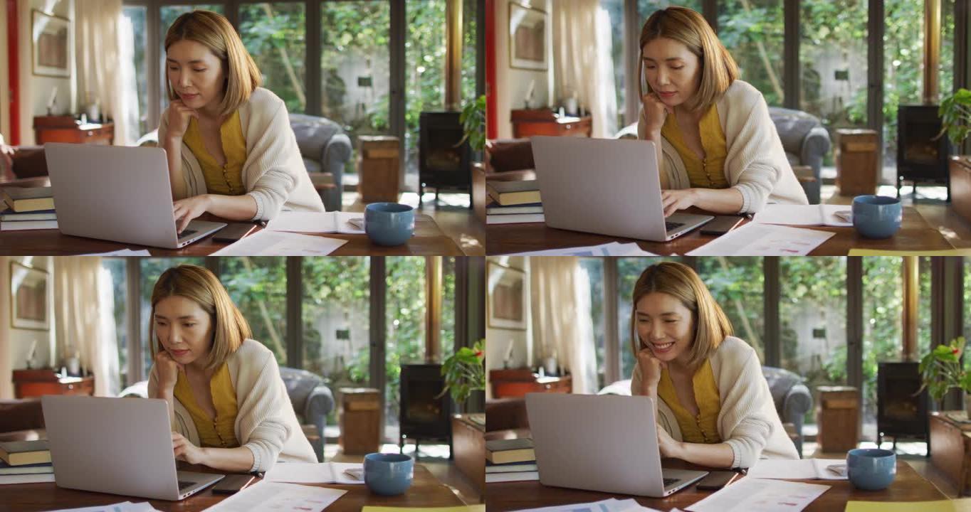 坐在餐桌旁在家工作并使用笔记本电脑的亚洲妇女