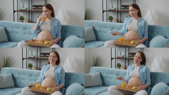 快乐的未来母亲在公寓里喝果汁和看电视的慢动作
