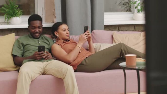 年轻的混血儿夫妇用智能手机在沙发上放松