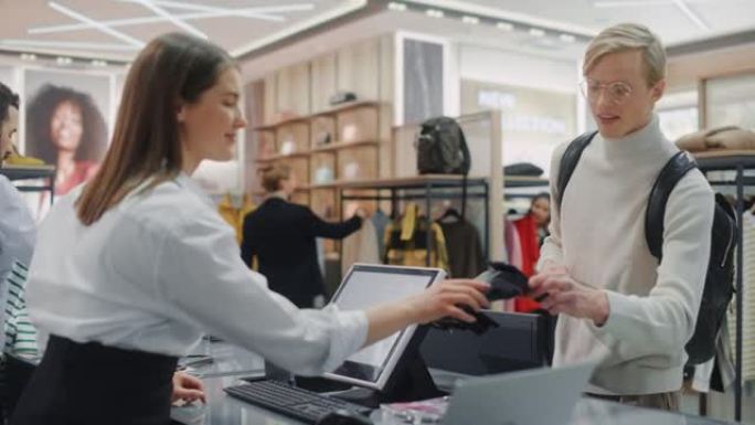 服装店: 收银台的年轻人购买使用非接触式NFC智能手机付款的衣服，友好的零售销售助手包装商品。设计师