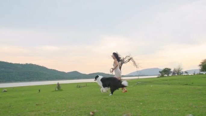 夏天，年轻女子在秋季公园的草坪上与边境牧羊犬一起奔跑。