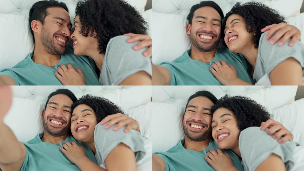 跨种族的夫妇在床上用手机自拍，在卧室放松的同时为社交媒体流媒体视频，在家里为幸福的婚姻微笑。漫画，爱