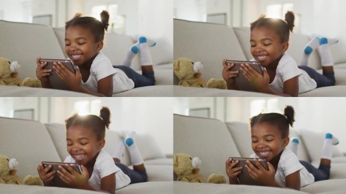 快乐的非洲裔美国女孩躺在沙发上在家使用数字平板电脑