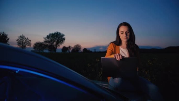 一个中年黑发女人坐在汽车引擎盖上时使用笔记本电脑的慢动作，背景为黄昏天空