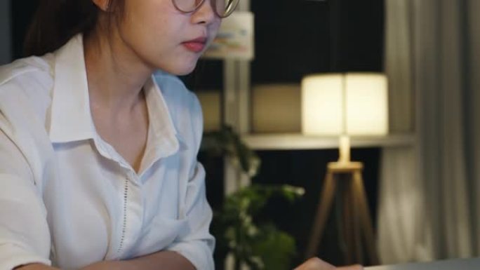 自由亚洲女士使用笔记本电脑在家里的客厅辛勤工作。