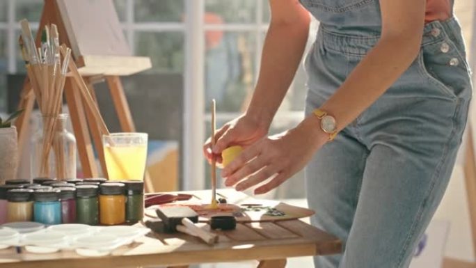 一位女画家在画室为绘画在调色板上涂漆的特写镜头。艺术家在车间工作时使用画笔混合颜色。女人为画布上的艺