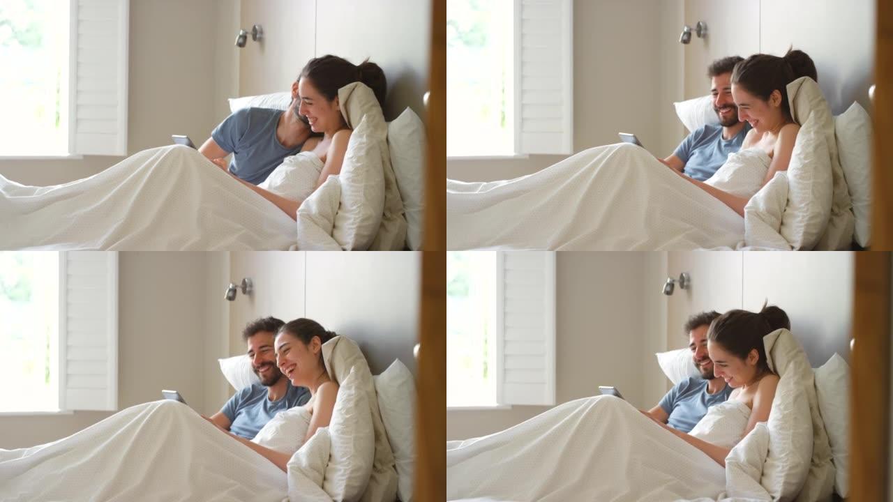 一对年轻夫妇在使用数字平板电脑时在床上深情的4k视频片段