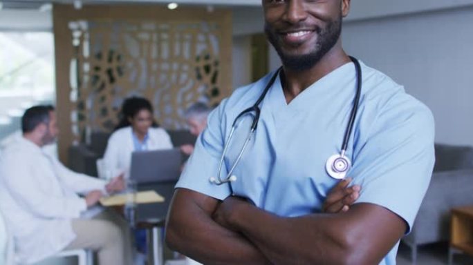 非洲裔美国男性医生微笑的肖像，背景中与同事讨论