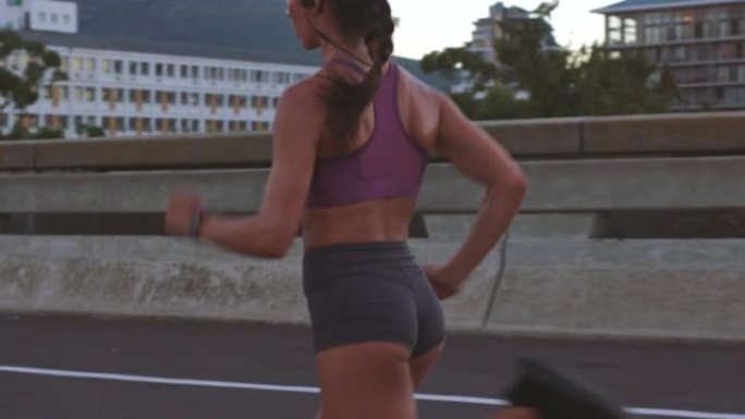 妇女在城市锻炼期间跑步，锻炼和健身，以促进健康和健康，同时用无线耳机听音乐。快速运动的女性在城市桥梁