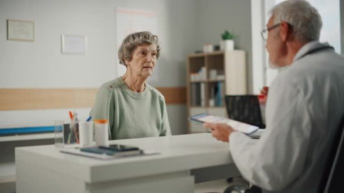 中年家庭医生与老年女病人在门诊会诊期间交谈。穿着白大褂的资深白种医生坐在医院办公室的电脑桌前。