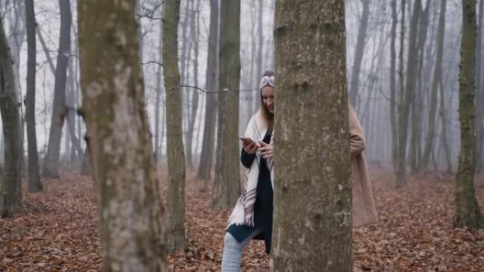 两个穿着保暖衣服的女人用手机在森林里散步