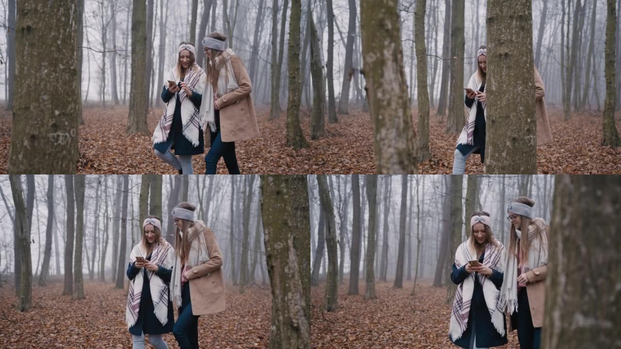 两个穿着保暖衣服的女人用手机在森林里散步