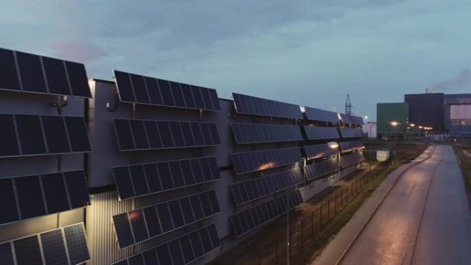 航空移动平行镜头，多个现代太阳能电池板连接到物流大楼的工业仓库。黄昏的天气和远处行驶的货车。