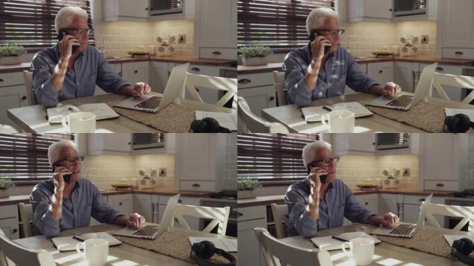 4k视频片段，一名高级男子独自坐在家里的厨房里使用技术