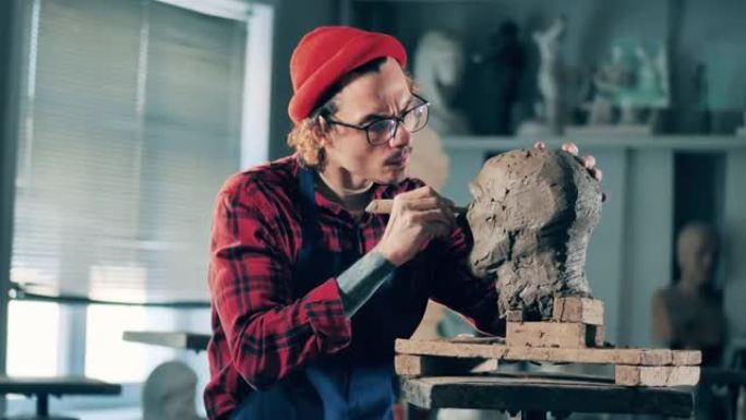男雕塑家正在工作室里固定一个粘土头。灵感，创造性的工作理念。