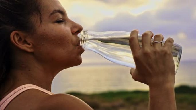 适合女运动员用玻璃水瓶喝水，站在海边的木板路上