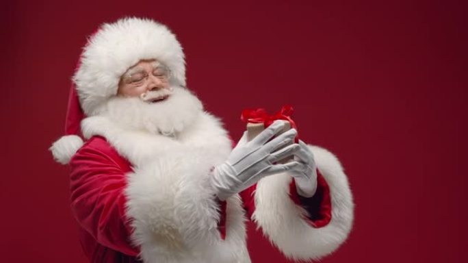 一位善良的圣诞老人向我们展示了一个可爱的小礼品盒，带着微笑，站在红色背景下，右边是复制品