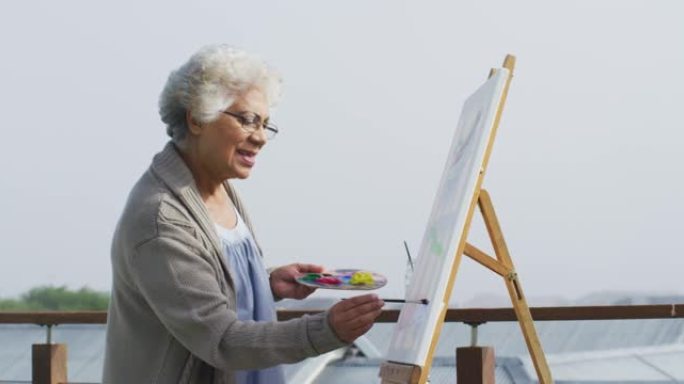 非裔美国高级妇女在家里阳台的画布上绘画