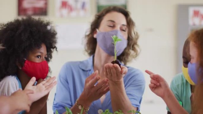 女教师戴口罩在课堂上向学生展示植物树苗
