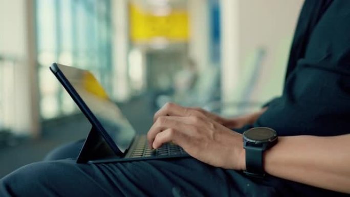 年轻的亚洲游客在等待登机时戴着黑色织物面具在数字平板电脑上打字。