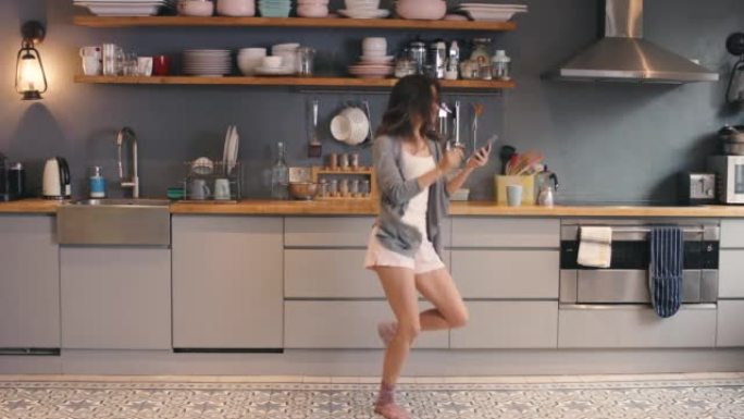 4k视频片段，一名年轻女子在家里的厨房里跳舞时使用电话