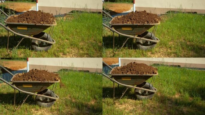 特写: 装满湿土的大型金属独轮车被推过后院。