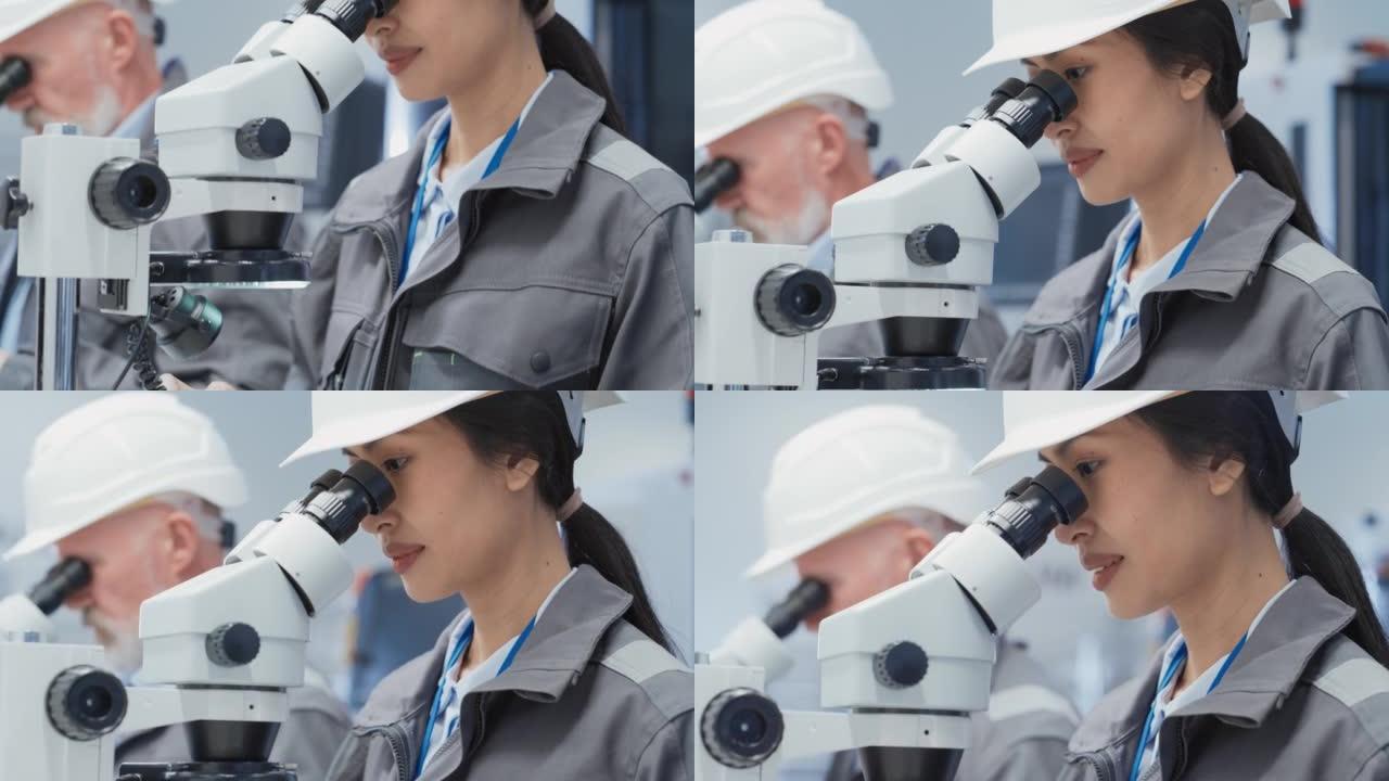 一位年轻的亚洲工业科学家戴着白色安全帽，在工厂的办公桌前工作，用显微镜检查制造生产零件的质量。