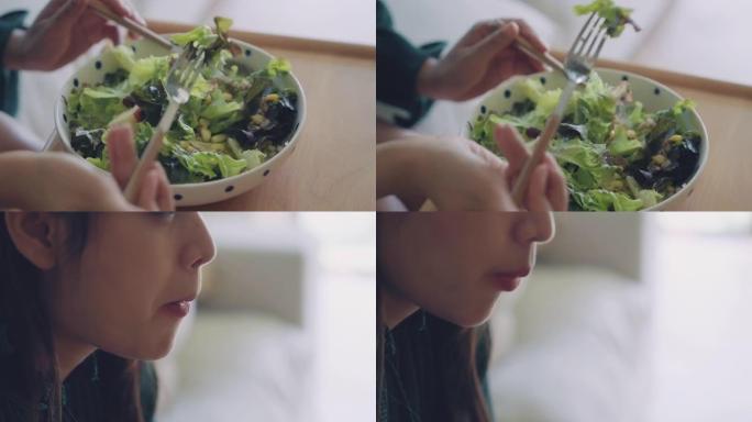 年轻快乐的亚洲女人坐在客厅的沙发上吃健康沙拉的特写镜头。