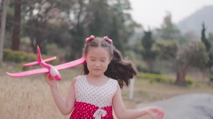 快乐的亚洲小女孩拿着玩具飞机在大麦田里奔跑