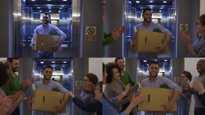 开朗的人们在办公室接待了新成员，因为他从电梯上下来，背着自己的物品看起来很高兴