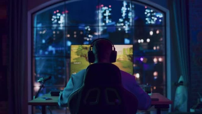 一个成功的非洲裔美国玩家戴上耳机，在家里霓虹灯照明的客厅里用个人电脑玩视频游戏的后角。胜利的年轻人。