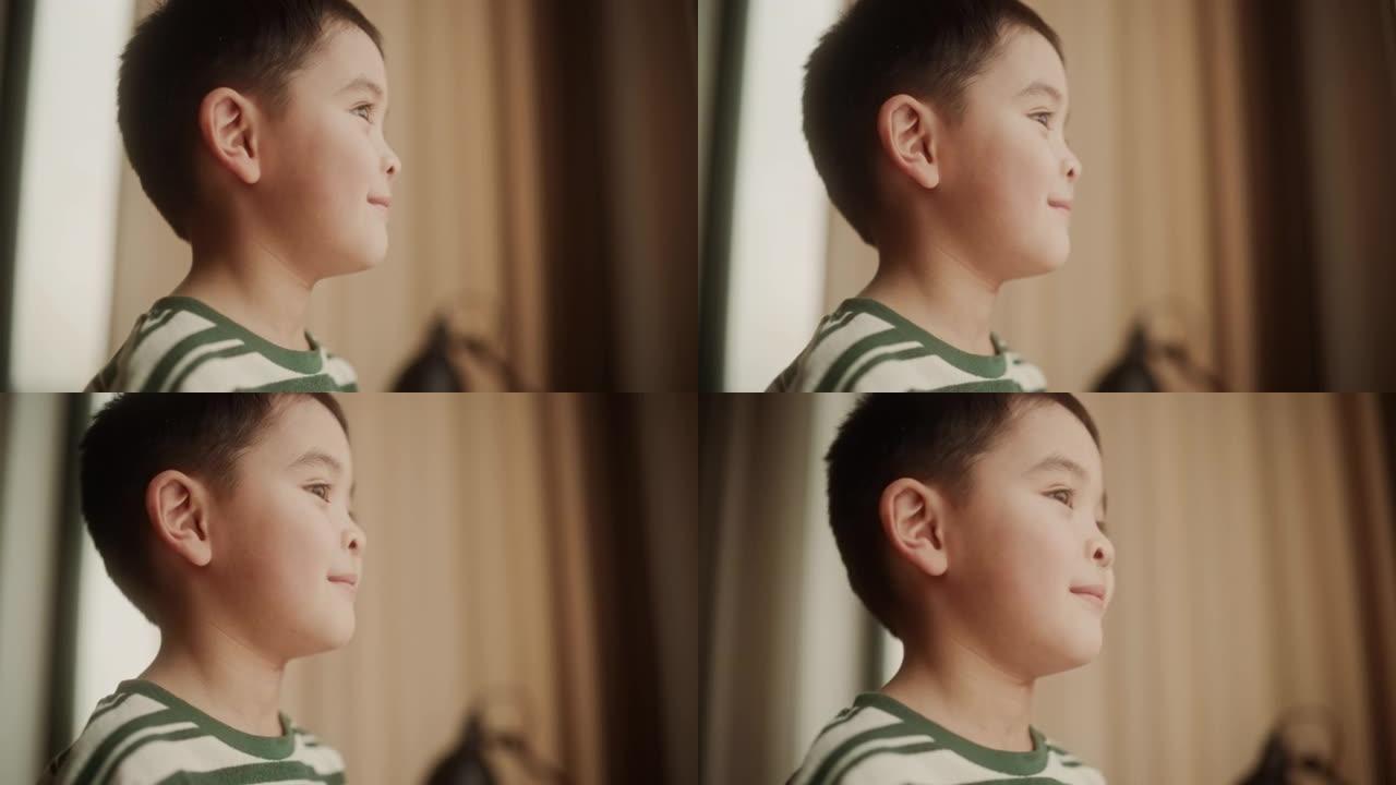 一个可爱的亚洲小男孩透过窗户微笑的肖像。自然点燃的肖像，一个快乐的男孩子梦想着伟大的梦想，眼睛充满了