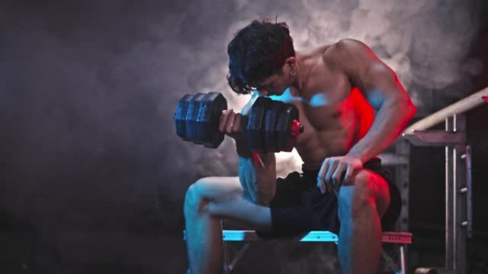 英俊的运动男子运动员在废弃的黑暗健身房用哑铃进行运动重量训练