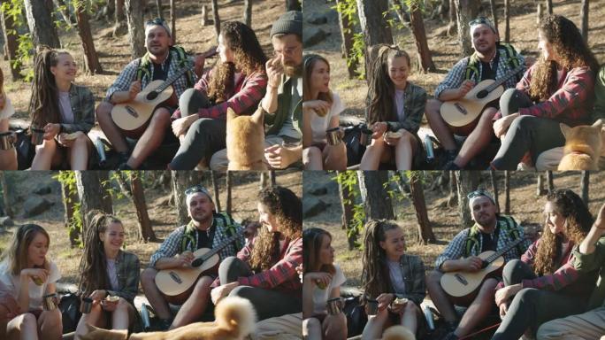 游客弹吉他和唱歌，而朋友在森林里喝酒和大笑与狗玩耍