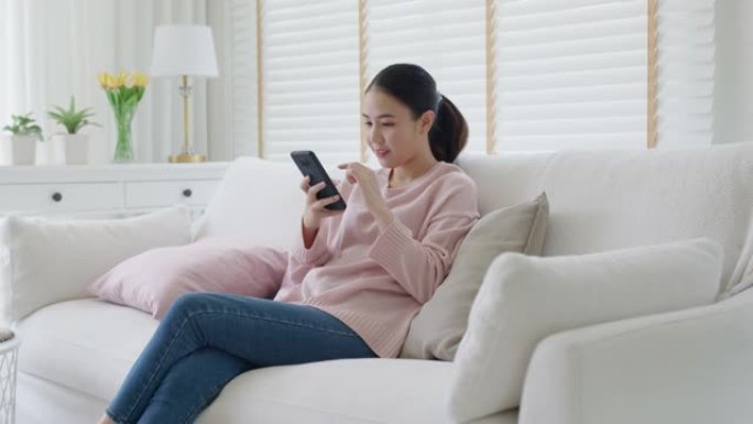 亚洲年轻女子在家沙发沙发上用手机在线购物。
