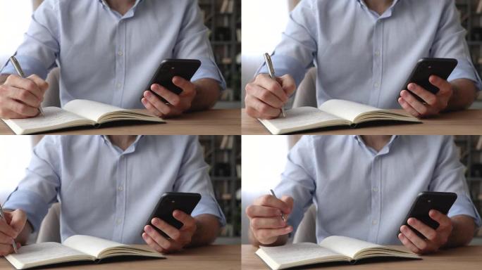 男人坐在桌子上，拿着智能手机在日记上写议程