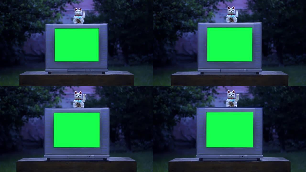 Maneki Neko幸运猫在绿屏的旧电视上。夜色。放大镜头。