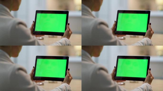一个女人拿着绿屏平板电脑在小工具上浏览互联网的后视图。数字平板电脑的特写镜头，在女商人的手中带有孤立