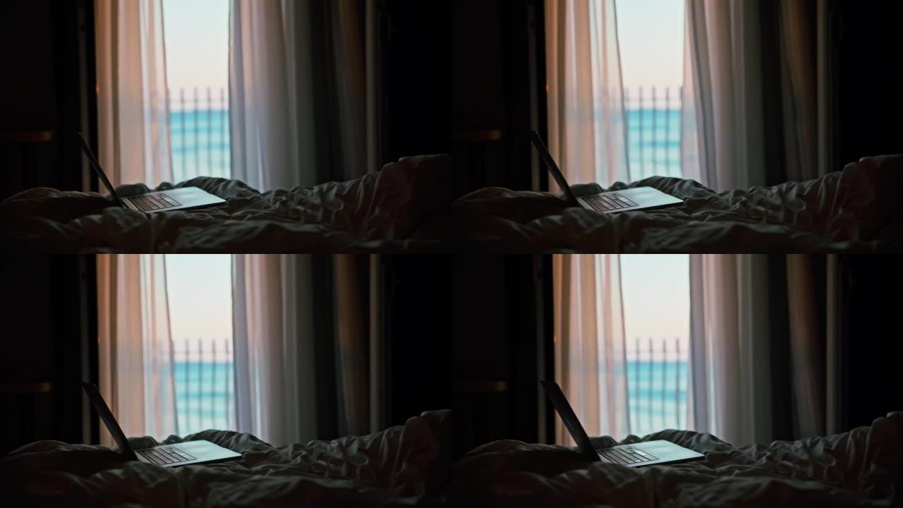 笔记本电脑站在酒店房间的床上，背景是阳台和海，透明的窗帘