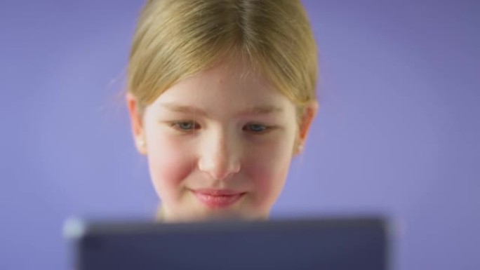 在紫色工作室背景下使用数字平板电脑拍摄微笑女孩的工作室照片-慢动作拍摄