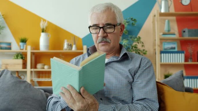 戴着眼镜的聪明老人独自在家躺在沙发上看书