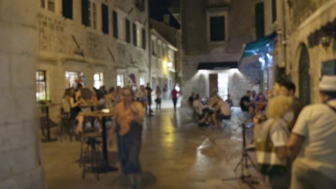 夏天晚上，人们在欧洲城镇的老中心散步的散焦镜头。街头咖啡馆有游客、交流、休息。舒适的浪漫氛围