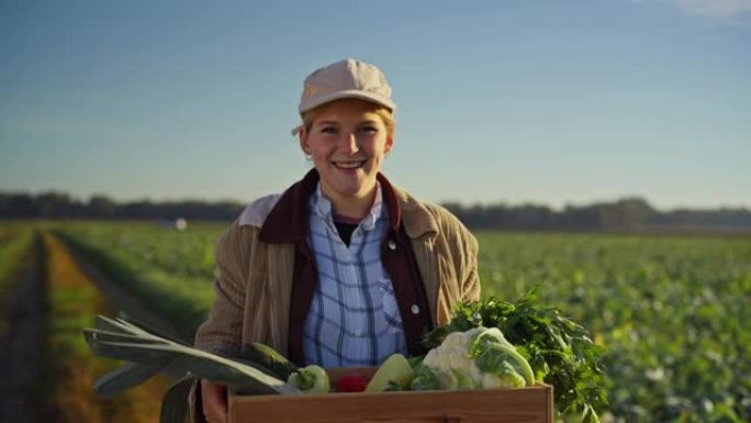 肖像快乐女农夫在阳光明媚的田野里搬运收获的蔬菜