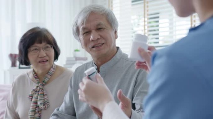年轻的护理人员穿着磨砂膏制服，向老年亚洲夫妇男女展示药瓶，上门护理服务。具有辅助生活药物监测概念的亚