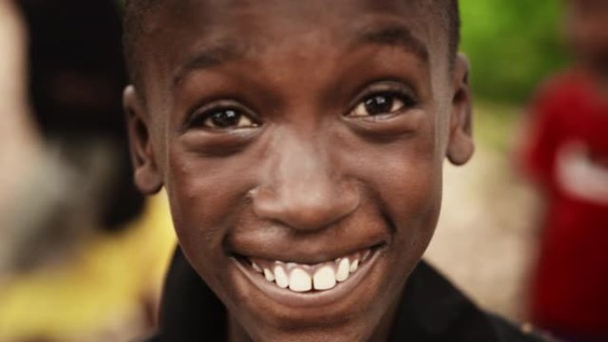 一个顽皮的真实的非洲孩子的特写肖像看着相机和微笑的强烈模糊的背景。快乐活力的黑人男孩与世界分享他美丽