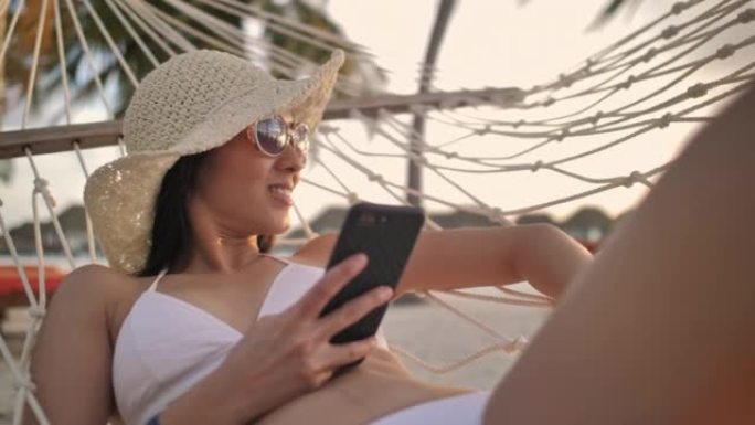 年轻女子在吊床上放松时使用智能手机