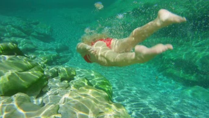 一个女人在暑假期间穿着红色泳衣在水下游泳。一个在大自然中度假的女人，在湖里游泳。一名身穿红色比基尼的