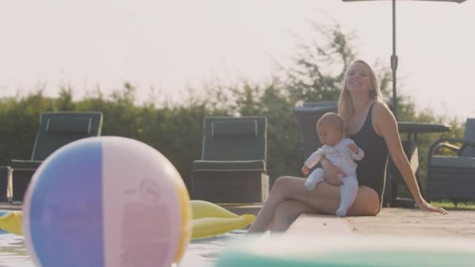 带着小女儿的母亲在暑假里坐在室外游泳池旁玩得开心