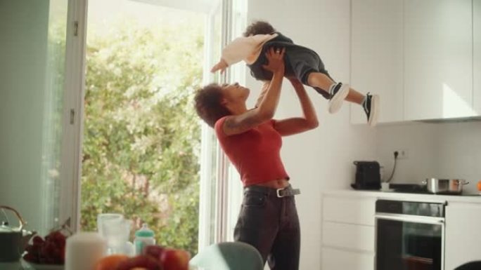 快乐的母亲抱着可爱的男婴，在现代家庭客厅玩耍，玩耍。拉丁女性举起并把蹒跚学步的孩子扔向空中。童年、新
